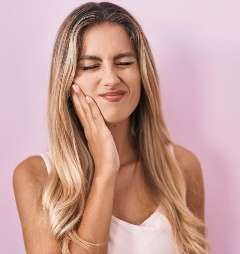 Woman cupping her jaw, wincing from sore gums